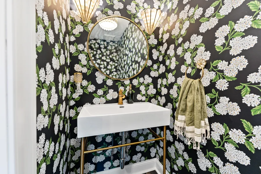 Powder room with floral wallpaper, a brass fan sconce and console sink