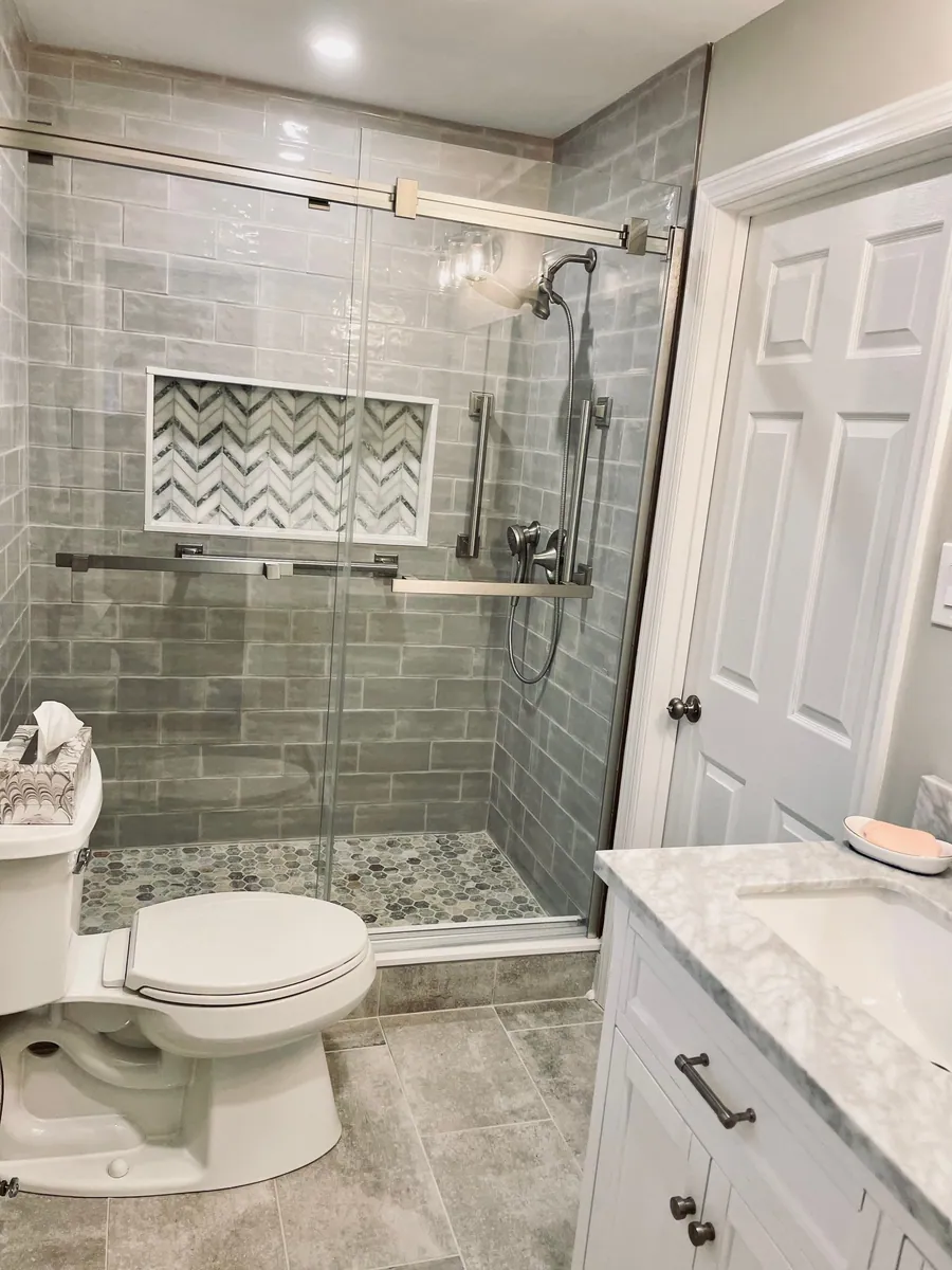 Grey tiled shower with a niche and glass door