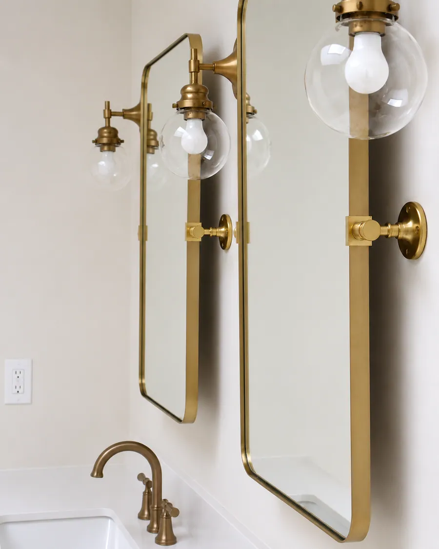 Double mirrors with brass sconces over a tiled wall