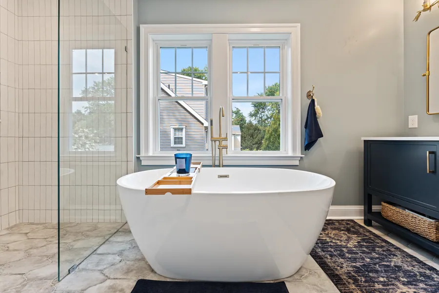 Freestanding tub next to a navy vanity and window