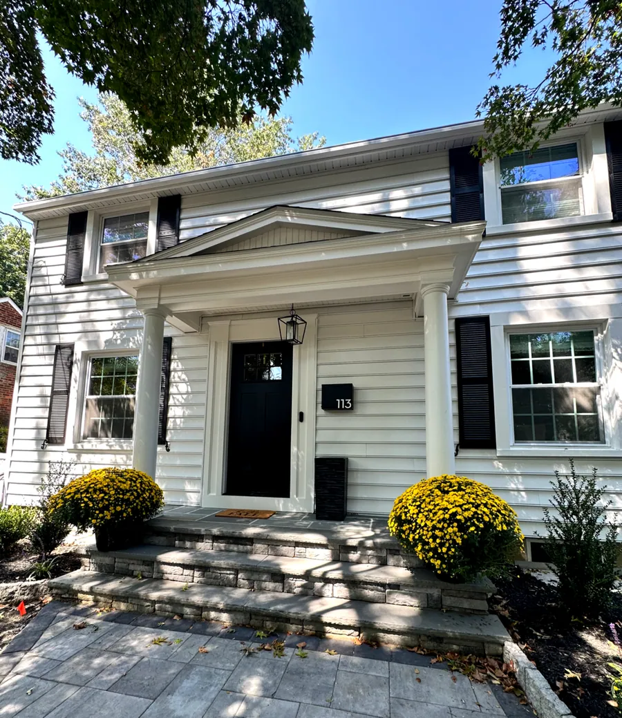 White colonial with black shutters and mums at the entry