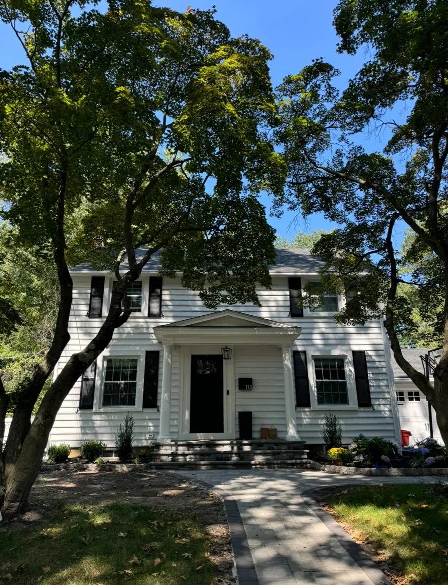 White colonial framed by a mature tree