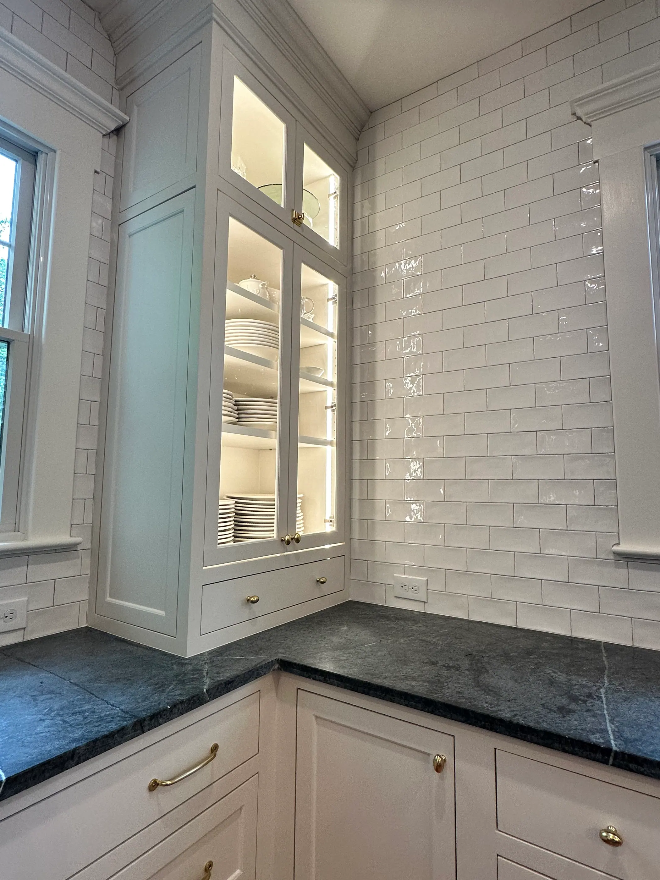 Corner glass cabinet above white subway tile