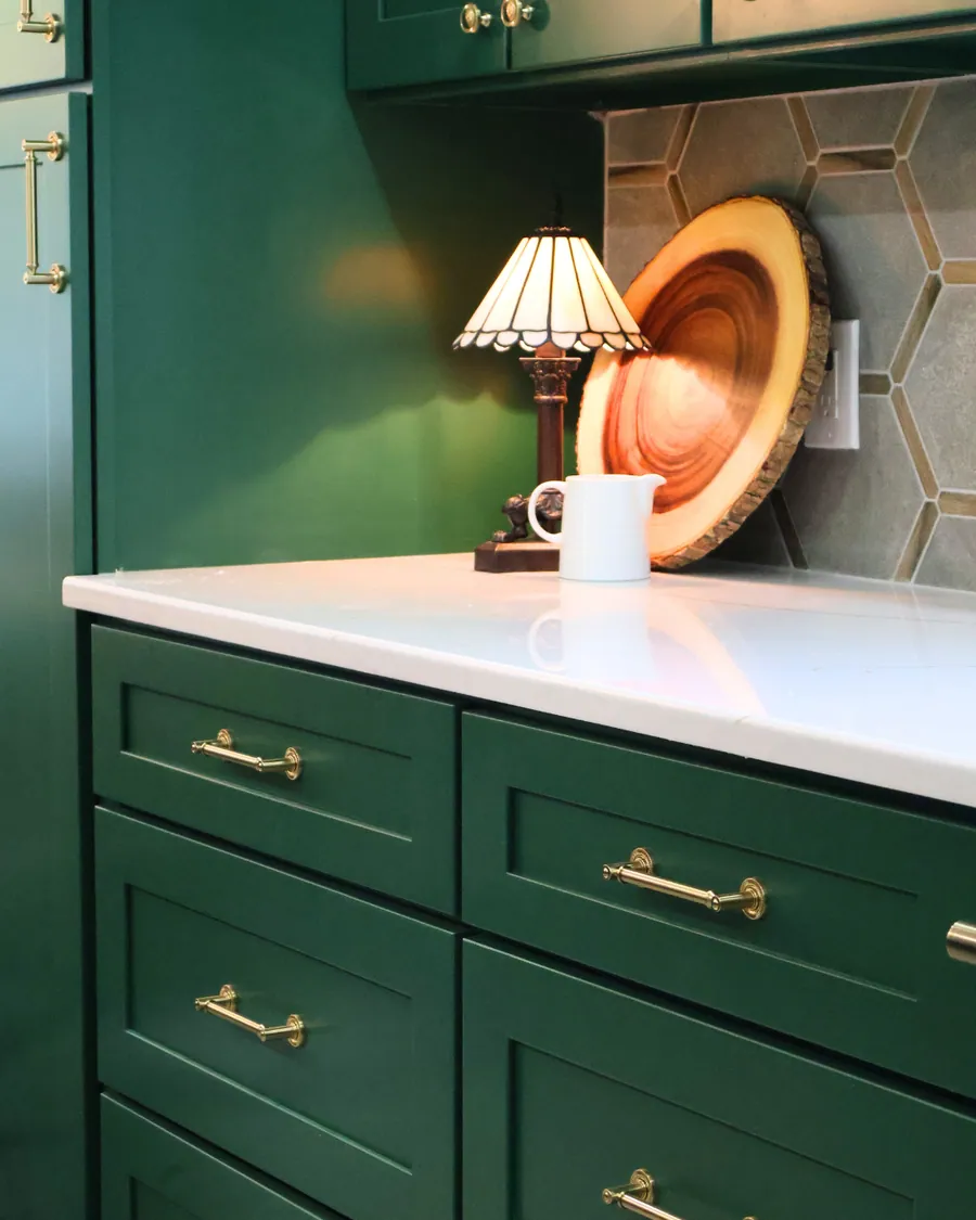 Green kitchen cabinetry with a brass lamp and open shelf