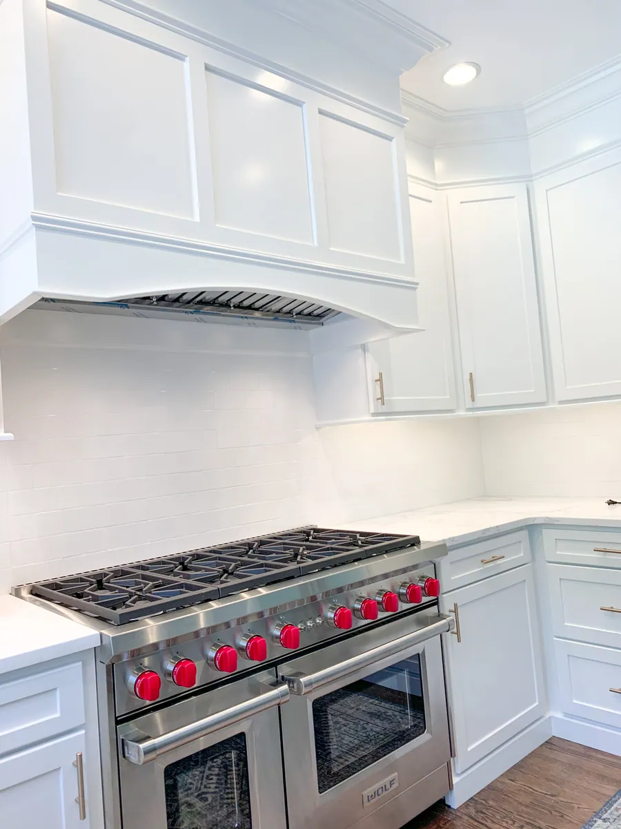 White kitchen with a custom hood beside a corner window