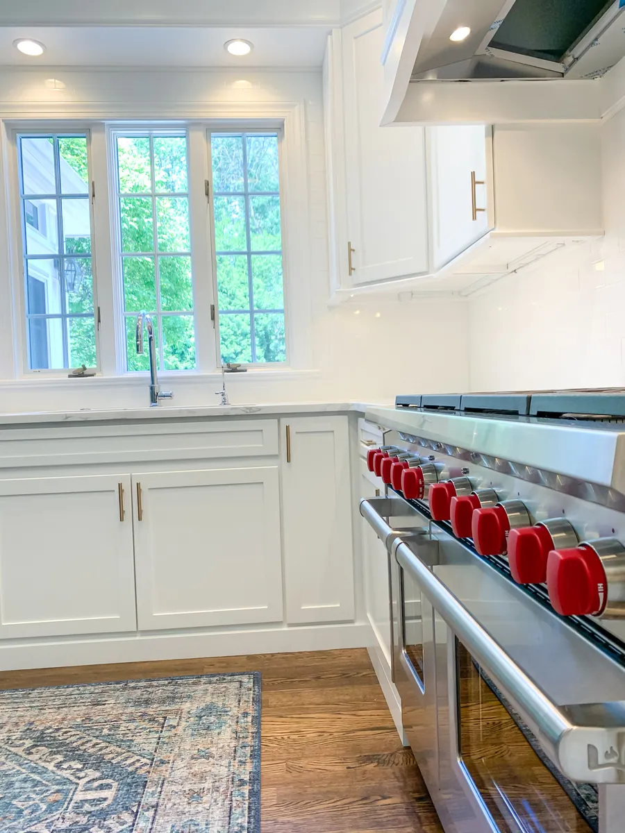 White kitchen with a red knob range and marble counters