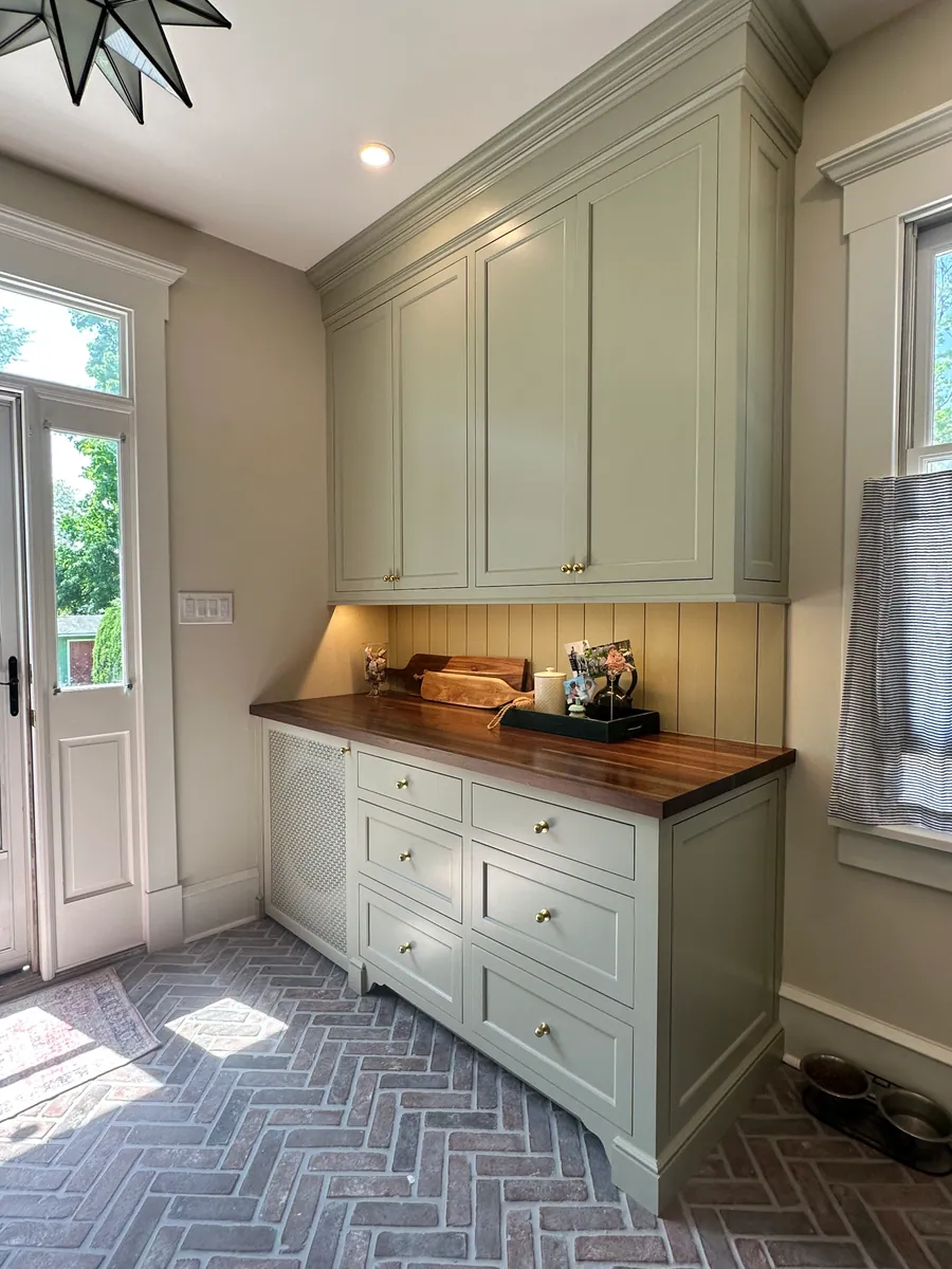 Sage pantry cabinetry with a walnut top over a brick floor