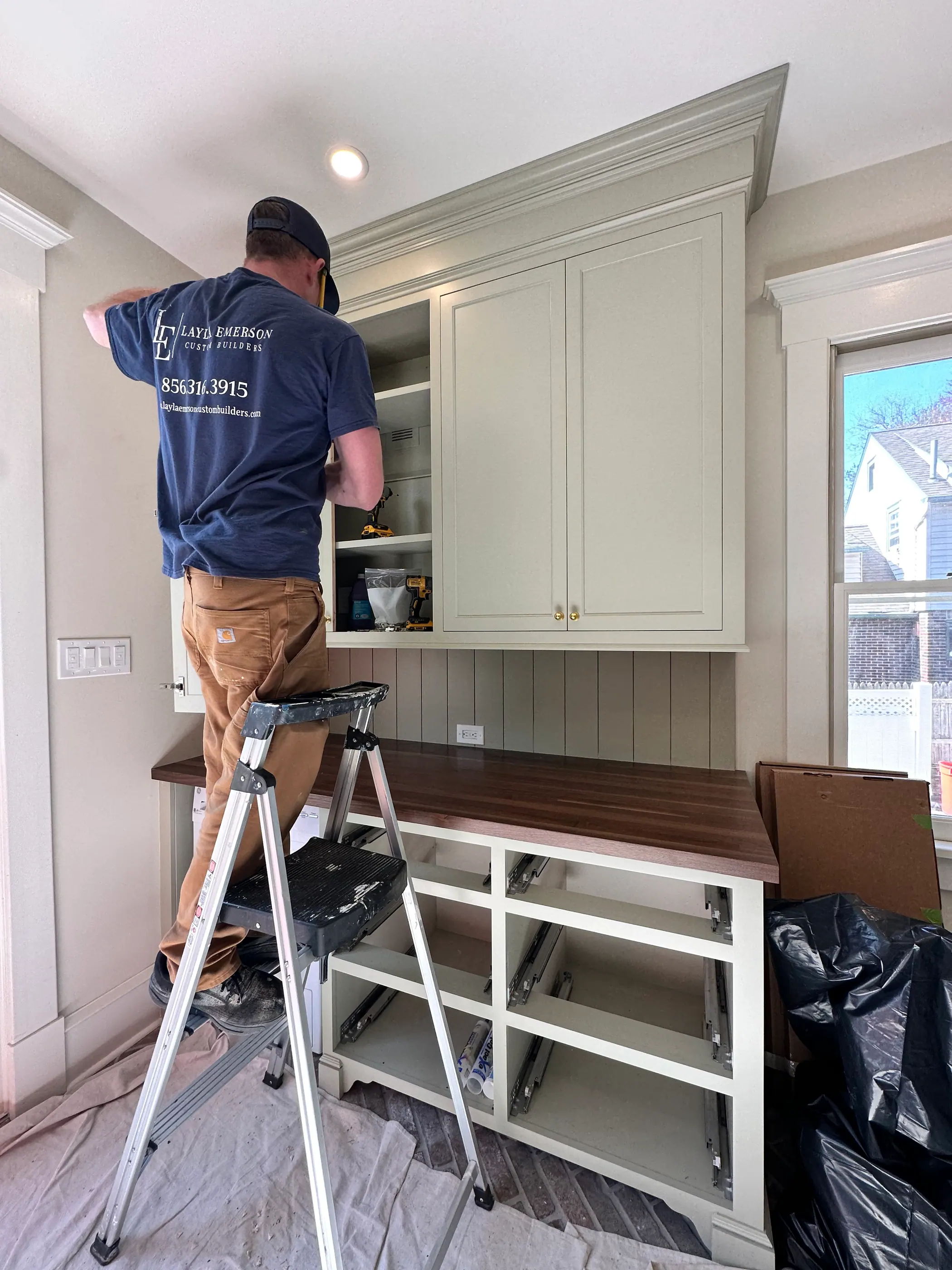 Carpenter installing upper cabinetry from a ladder