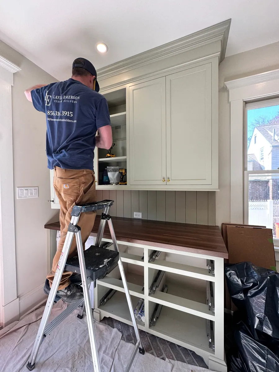 Carpenter installing upper cabinetry from a ladder